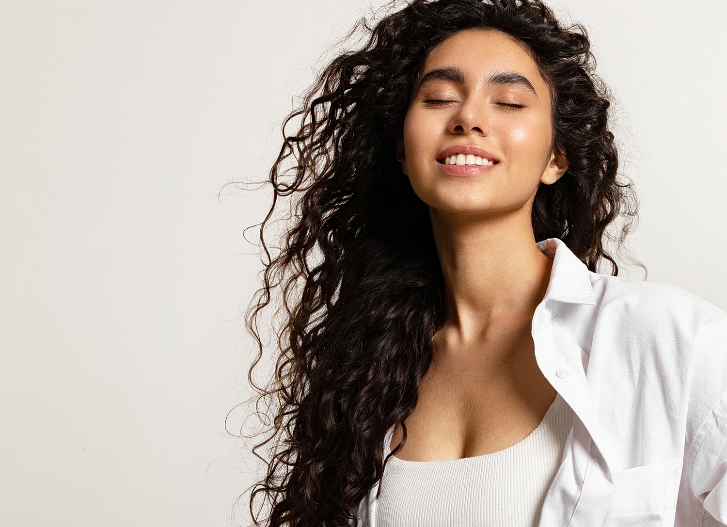 Woman with curly hair smiling against neutral background.