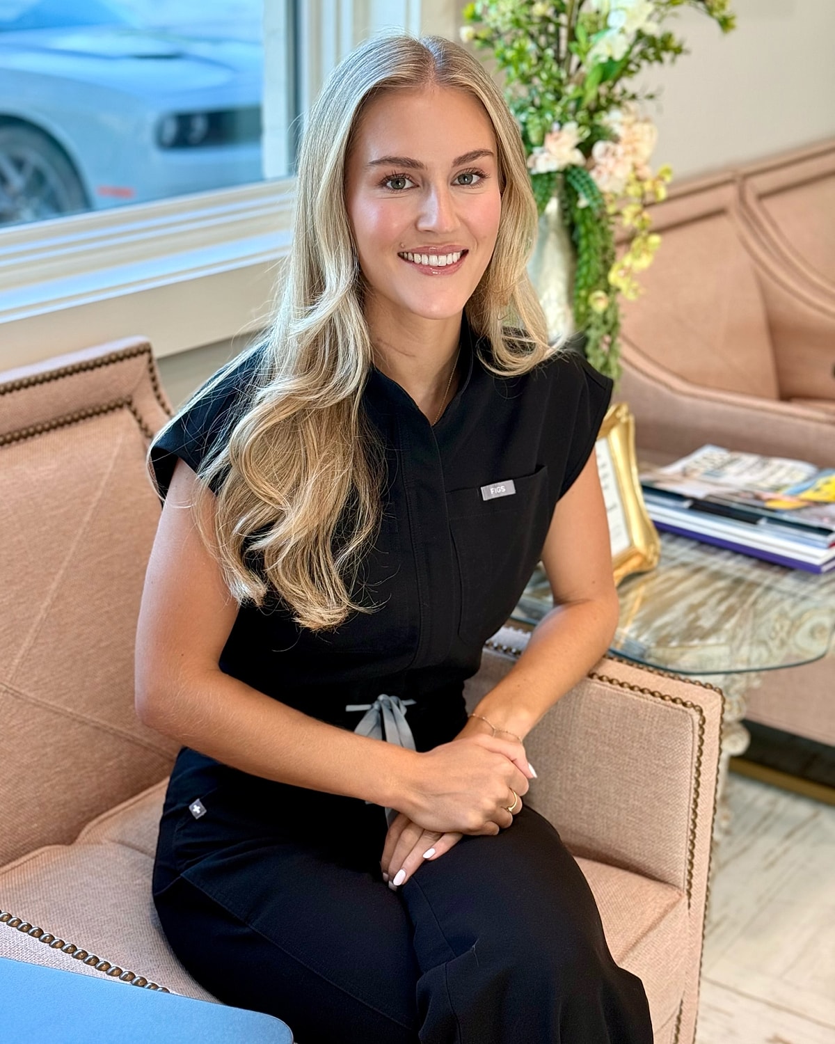 Woman in black attire smiling, seated indoors.